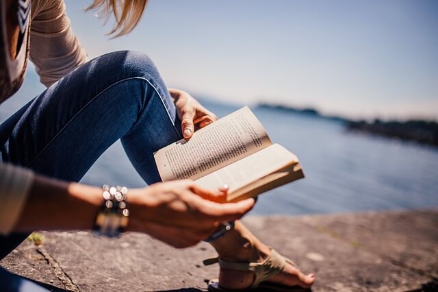 Kobieta siedzi nad morzem i czyta książkę