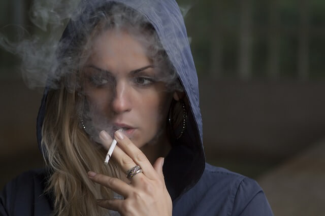 Kobieta w bluzie z kapturem pali papierosa