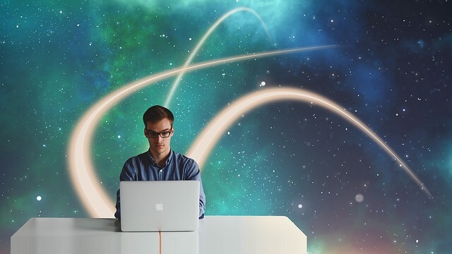 Mężczyzna siedzi przy laptopie na tle galaktyki