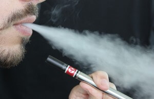 mężczyzna pali elektronicznego papierosa i wypuszcza dym